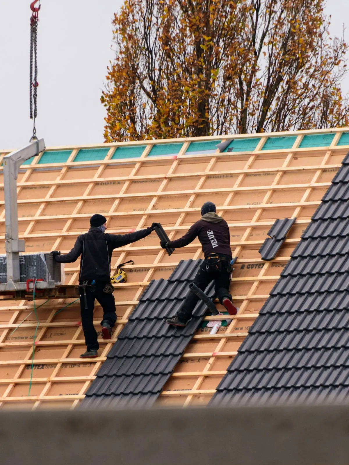 Due posatori al lavoro sul rifacimento di un tetto a falde, durante la posa delle tegole